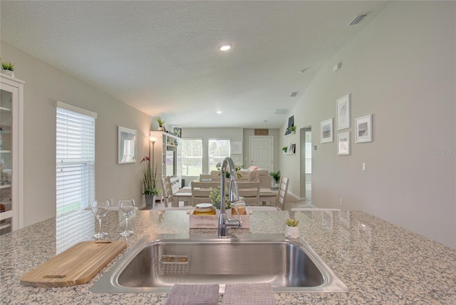 kitchen featuring visible vents, lofted ceiling, open floor plan, a textured ceiling, and a sink