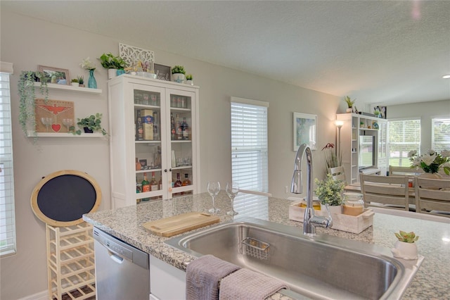 kitchen with light stone counters, a sink, white cabinets, stainless steel dishwasher, and open shelves