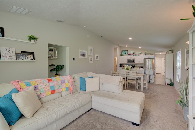 living room featuring lofted ceiling, a textured ceiling, visible vents, and light colored carpet