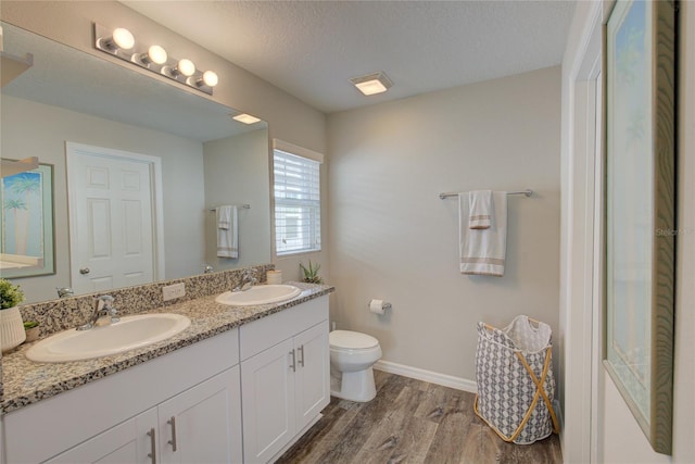 bathroom with double vanity, a sink, toilet, and wood finished floors