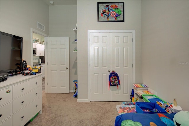 bedroom with baseboards, visible vents, light colored carpet, a high ceiling, and a closet