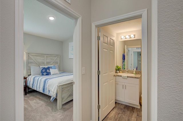 bedroom featuring a textured wall, light carpet, a sink, and light wood-style flooring