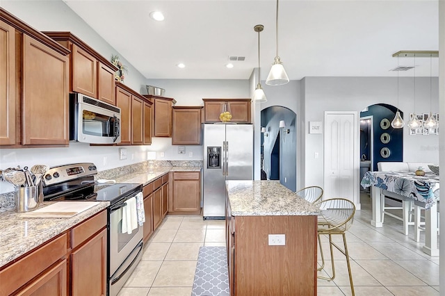 kitchen featuring stainless steel appliances, pendant lighting, a center island, light stone counters, and light tile patterned floors