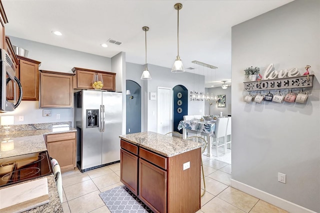 kitchen featuring light tile patterned floors, a center island, ceiling fan, light stone countertops, and appliances with stainless steel finishes