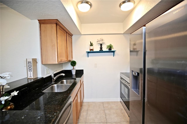 kitchen featuring sink, light tile patterned floors, stainless steel appliances, and dark stone counters