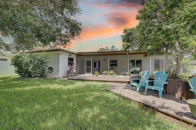 back house at dusk featuring a lawn and a deck