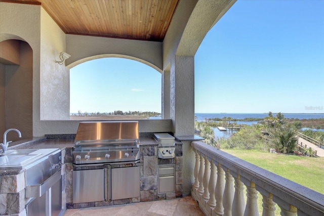 view of patio with a balcony, a water view, area for grilling, and an outdoor kitchen