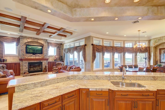 kitchen with a fireplace, hanging light fixtures, sink, coffered ceiling, and light stone counters