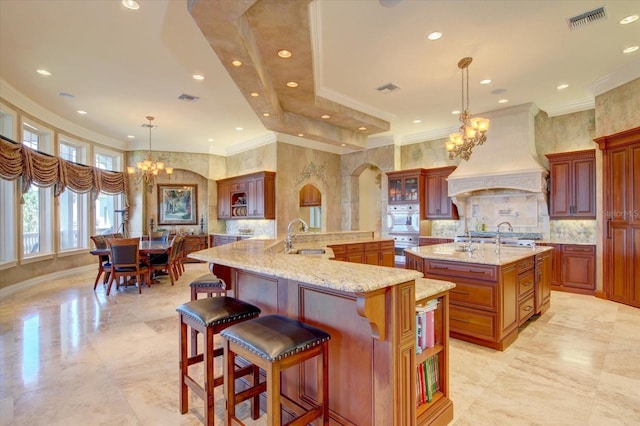 kitchen with a breakfast bar area, an inviting chandelier, premium range hood, decorative light fixtures, and a large island with sink