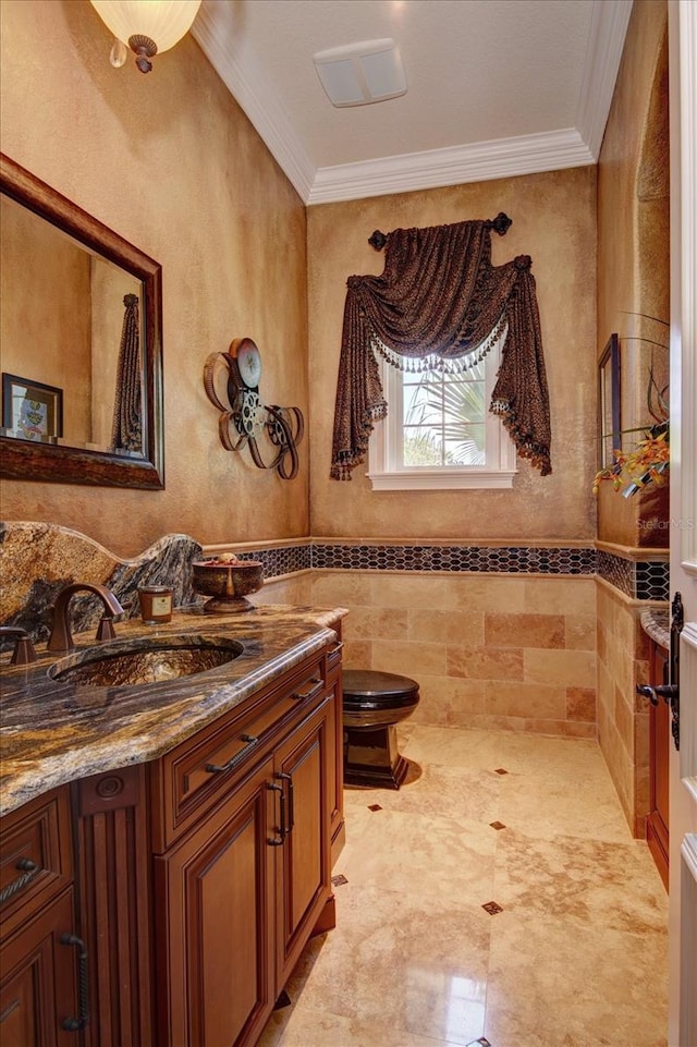 bathroom featuring tile patterned flooring, crown molding, toilet, vanity, and tile walls