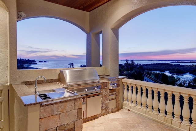 patio terrace at dusk featuring area for grilling, an outdoor kitchen, and a water view