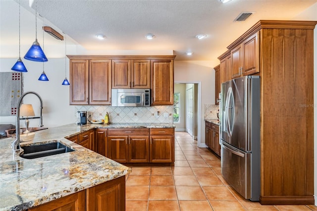 kitchen with brown cabinets, a peninsula, light stone countertops, stainless steel appliances, and a sink