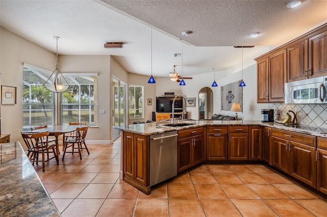 kitchen featuring arched walkways, appliances with stainless steel finishes, decorative light fixtures, a peninsula, and backsplash