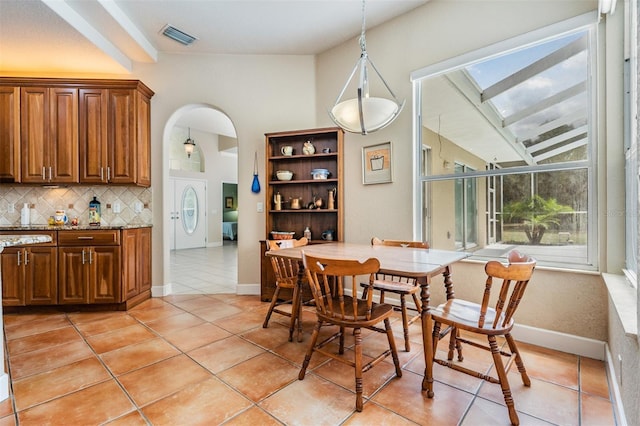 dining room featuring light tile patterned floors, baseboards, visible vents, and arched walkways