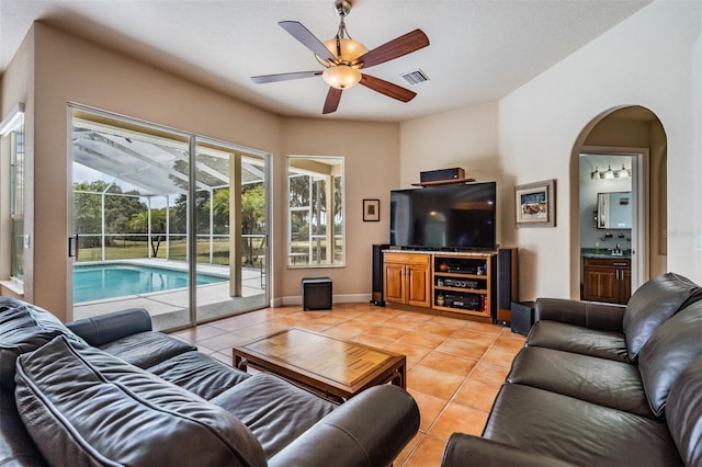living area with arched walkways, light tile patterned flooring, visible vents, baseboards, and a ceiling fan