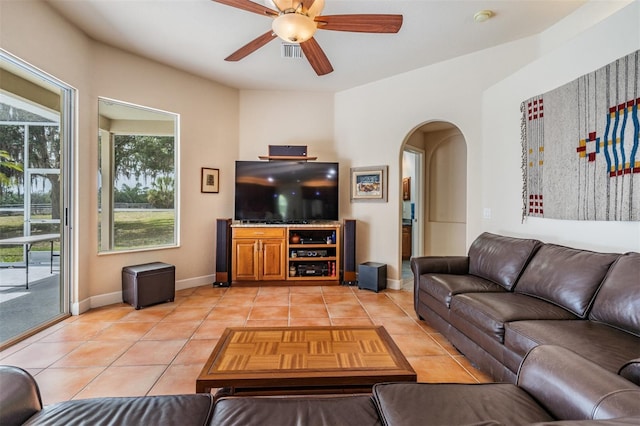 living area featuring arched walkways, visible vents, a ceiling fan, light tile patterned flooring, and baseboards
