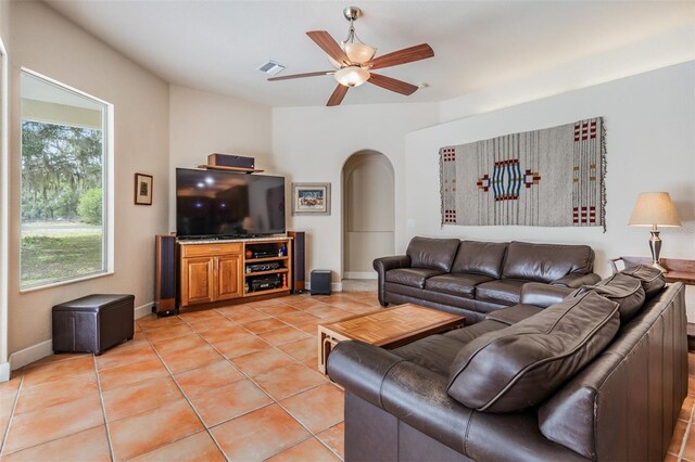 living area with arched walkways, light tile patterned floors, visible vents, ceiling fan, and baseboards