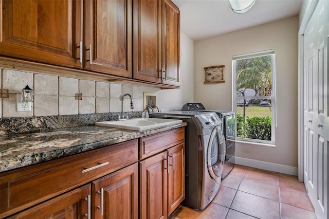 washroom with cabinet space, light tile patterned floors, baseboards, washing machine and dryer, and a sink