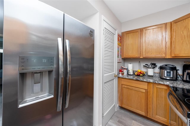 kitchen featuring dark stone countertops, light hardwood / wood-style flooring, and appliances with stainless steel finishes