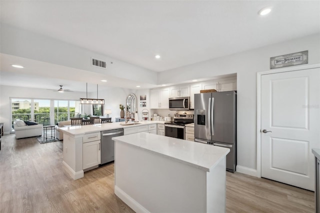 kitchen with appliances with stainless steel finishes, kitchen peninsula, pendant lighting, light hardwood / wood-style floors, and white cabinets