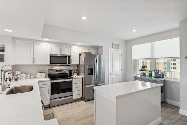 kitchen featuring sink, light hardwood / wood-style flooring, appliances with stainless steel finishes, white cabinetry, and light stone countertops