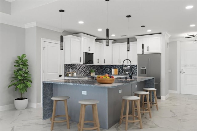 kitchen featuring white cabinets, a kitchen island with sink, dark stone countertops, and a breakfast bar area