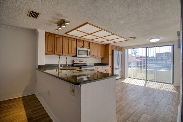 kitchen featuring sink, dark stone countertops, kitchen peninsula, stainless steel appliances, and a textured ceiling