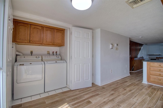 laundry room with a textured ceiling, light hardwood / wood-style flooring, cabinets, and washer and dryer