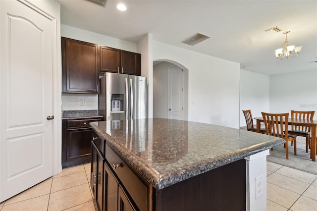 kitchen with a kitchen island, stainless steel fridge, dark stone counters, hanging light fixtures, and light tile patterned floors