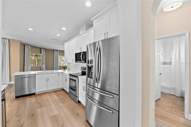 kitchen with white cabinets, kitchen peninsula, appliances with stainless steel finishes, and light hardwood / wood-style flooring