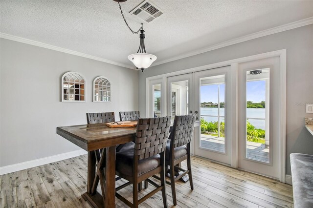 dining room featuring light hardwood / wood-style floors, a water view, a textured ceiling, and crown molding