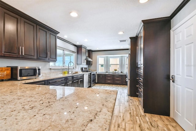 kitchen with light hardwood / wood-style flooring, stainless steel appliances, light stone counters, dark brown cabinetry, and ornamental molding