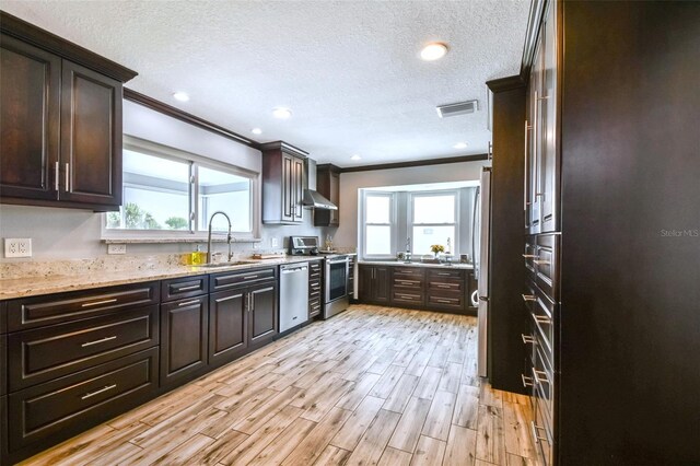 kitchen with light wood-type flooring, light stone counters, stainless steel dishwasher, stove, and sink