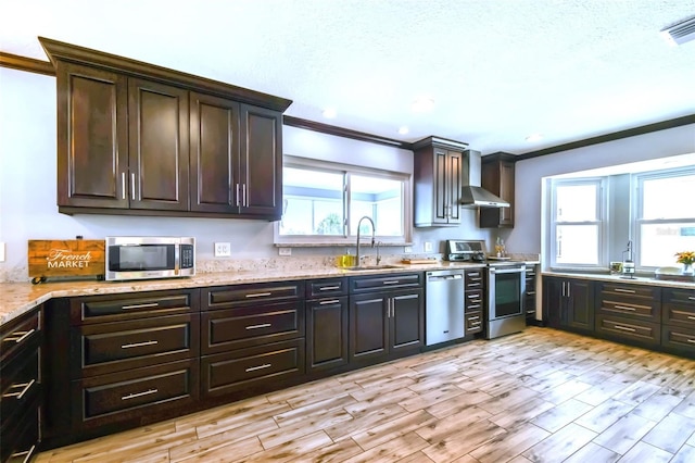 kitchen with a healthy amount of sunlight, appliances with stainless steel finishes, wall chimney exhaust hood, and dark brown cabinets