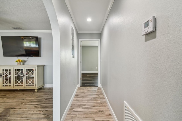 hallway with crown molding, light wood-type flooring, and a textured ceiling