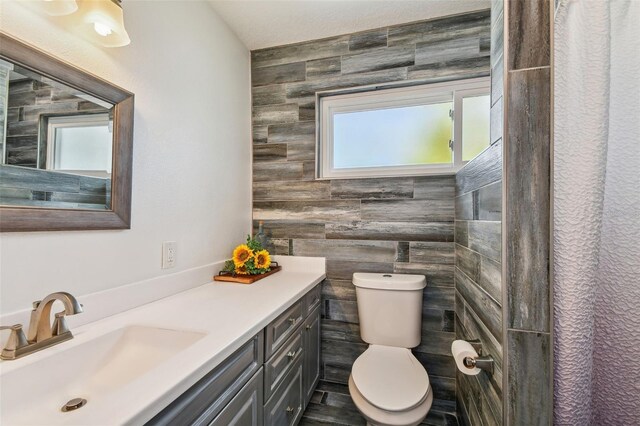 bathroom with vanity, toilet, plenty of natural light, and tile walls