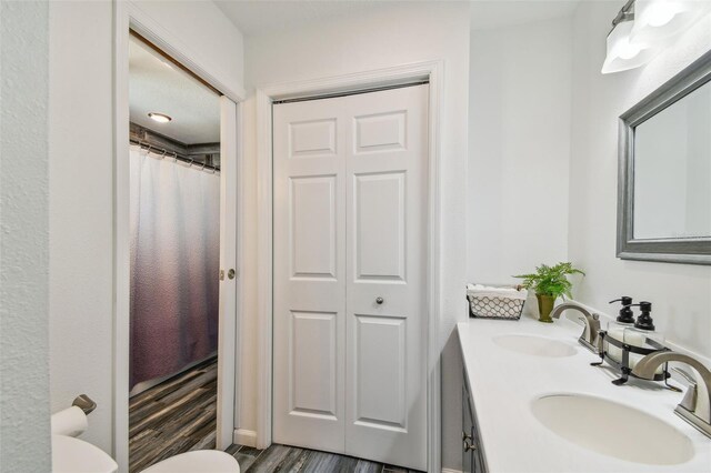 bathroom with dual vanity, toilet, and hardwood / wood-style floors