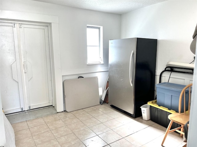 kitchen with stainless steel fridge, light tile patterned floors, and a textured ceiling