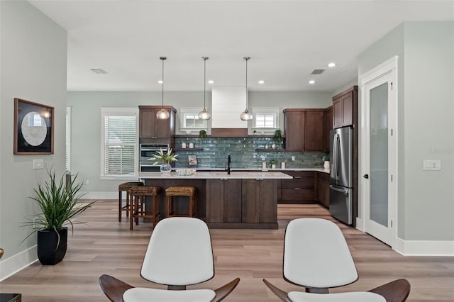 kitchen with tasteful backsplash, stainless steel refrigerator, pendant lighting, a healthy amount of sunlight, and a center island with sink