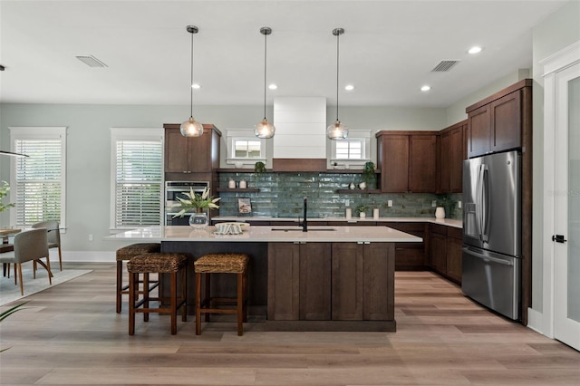 kitchen featuring decorative backsplash, dark brown cabinetry, light hardwood / wood-style flooring, pendant lighting, and stainless steel fridge