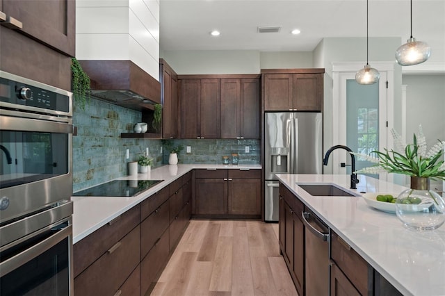 kitchen with appliances with stainless steel finishes, decorative light fixtures, sink, backsplash, and light wood-type flooring