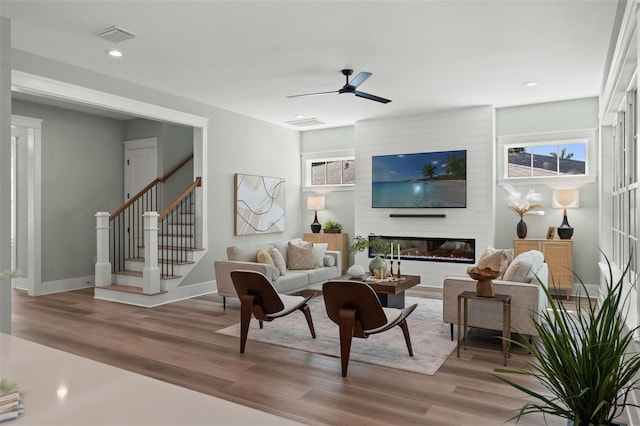 living room featuring ceiling fan, a large fireplace, and hardwood / wood-style floors