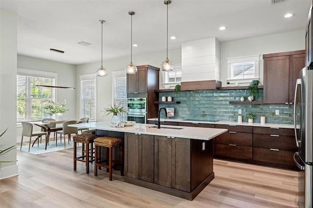 kitchen with appliances with stainless steel finishes, sink, decorative light fixtures, backsplash, and a center island with sink