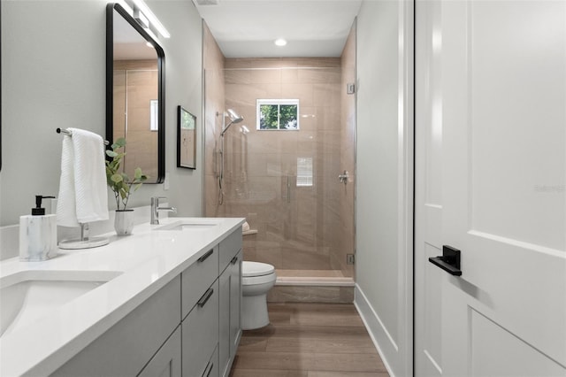 bathroom with hardwood / wood-style floors, toilet, a shower with shower door, and vanity