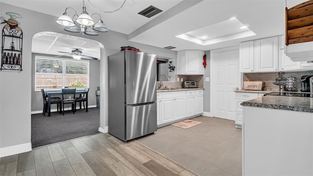 kitchen with pendant lighting, white cabinets, stainless steel fridge, decorative backsplash, and a raised ceiling