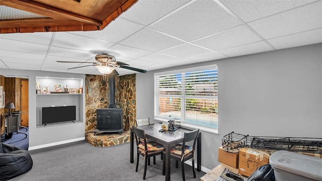 carpeted dining space with a wood stove, a drop ceiling, and ceiling fan