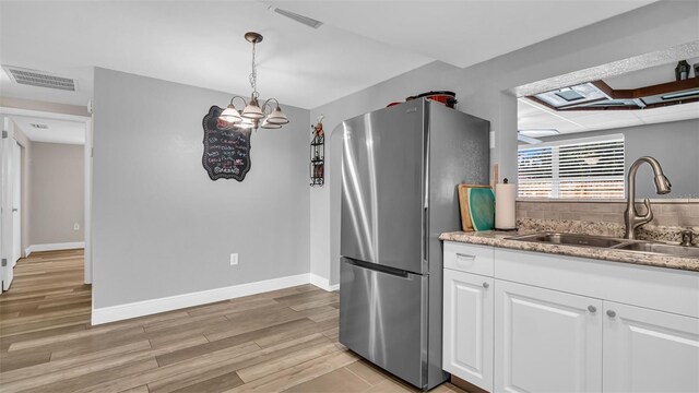 kitchen featuring sink, white cabinetry, hanging light fixtures, stainless steel fridge, and light hardwood / wood-style floors