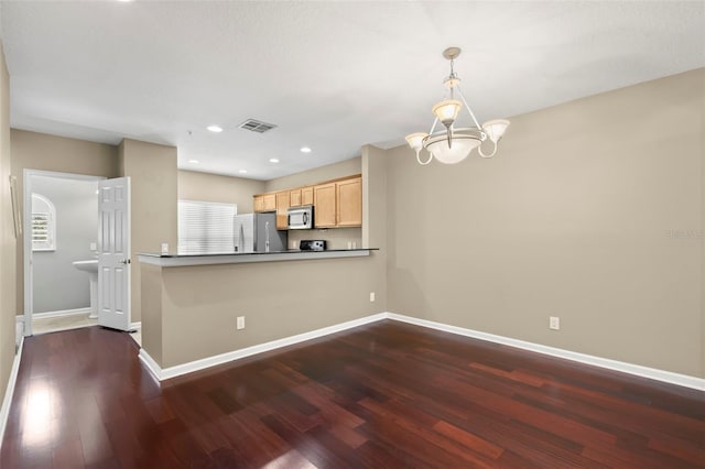 kitchen featuring appliances with stainless steel finishes, hanging light fixtures, kitchen peninsula, dark wood-type flooring, and light brown cabinets