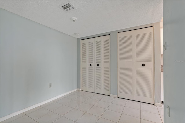 unfurnished bedroom featuring multiple closets, light tile patterned floors, and a textured ceiling