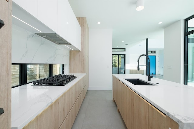 kitchen with light tile patterned floors, sink, light stone counters, stainless steel gas cooktop, and white cabinetry